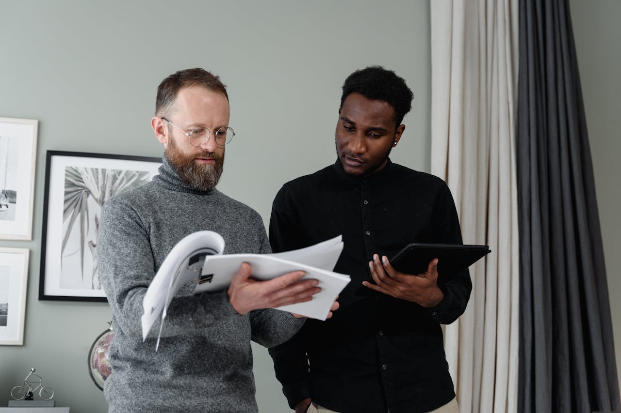 Two businessmen analyzing documents and using a tablet in a modern office setting.